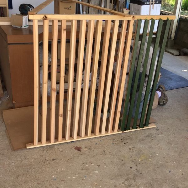 DIY木製フェンスの杉材を塗装している写真。カットした木材を並べて塗っている様子。作業中の木材が見える。