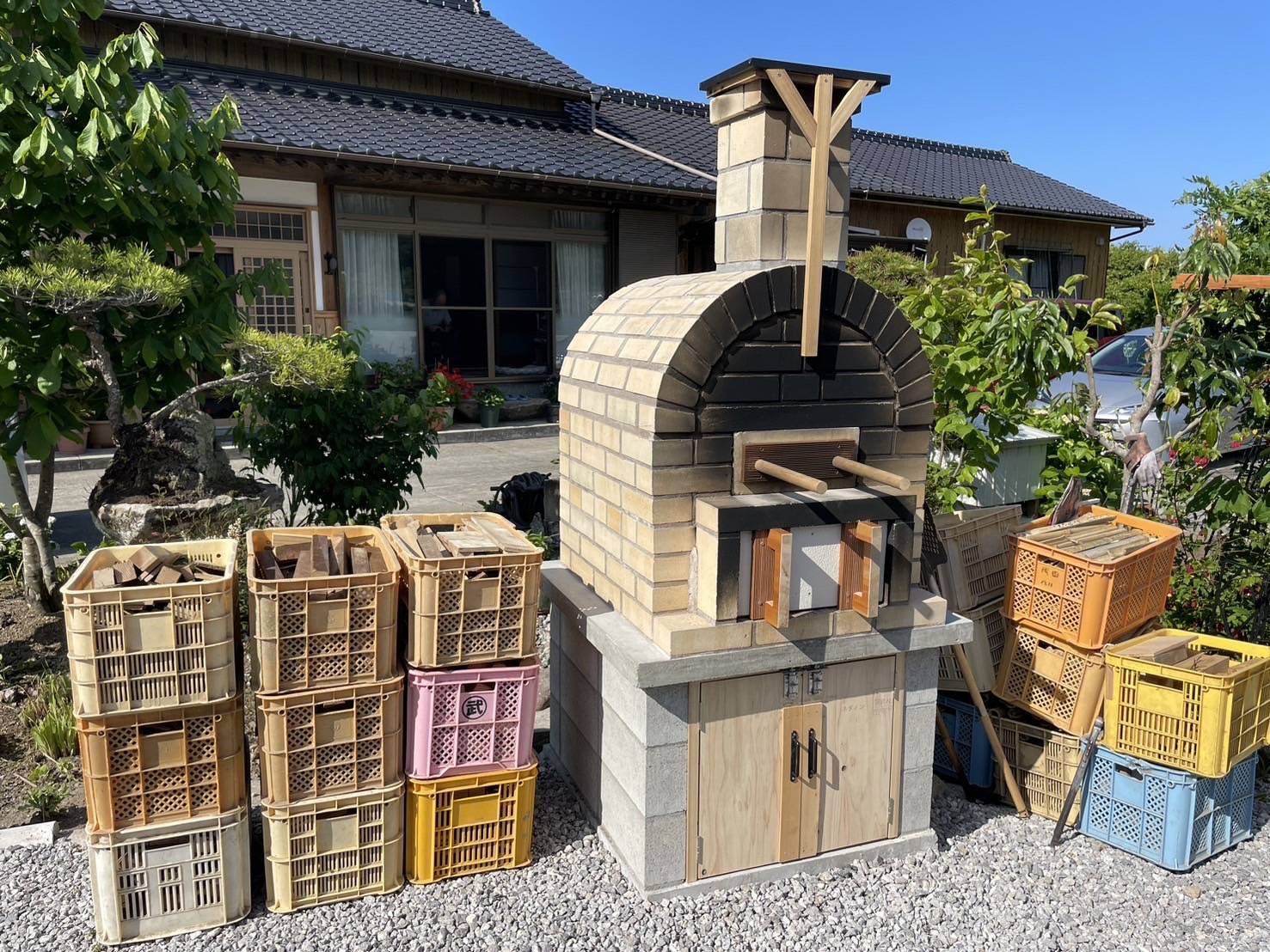 成したピザ窯の横で、お客様にピザ窯用の薪をプレゼントしている様子。国東市の外構リフォーム事例