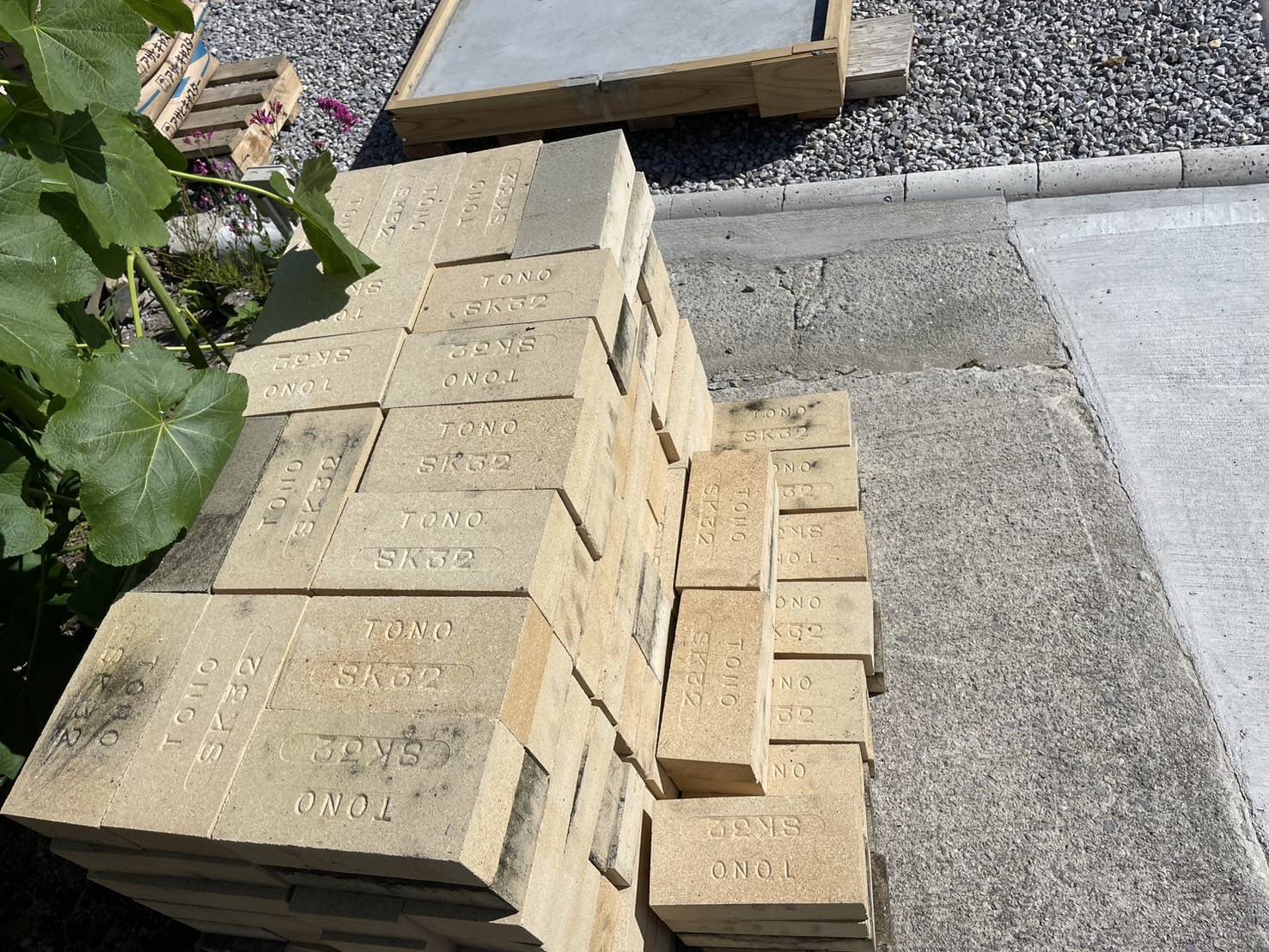 国東市でのピザ窯設置工事のため、高品質なSK32耐火レンガがトラックから降ろされている写真。職人がレンガを運ぶ作業風景。