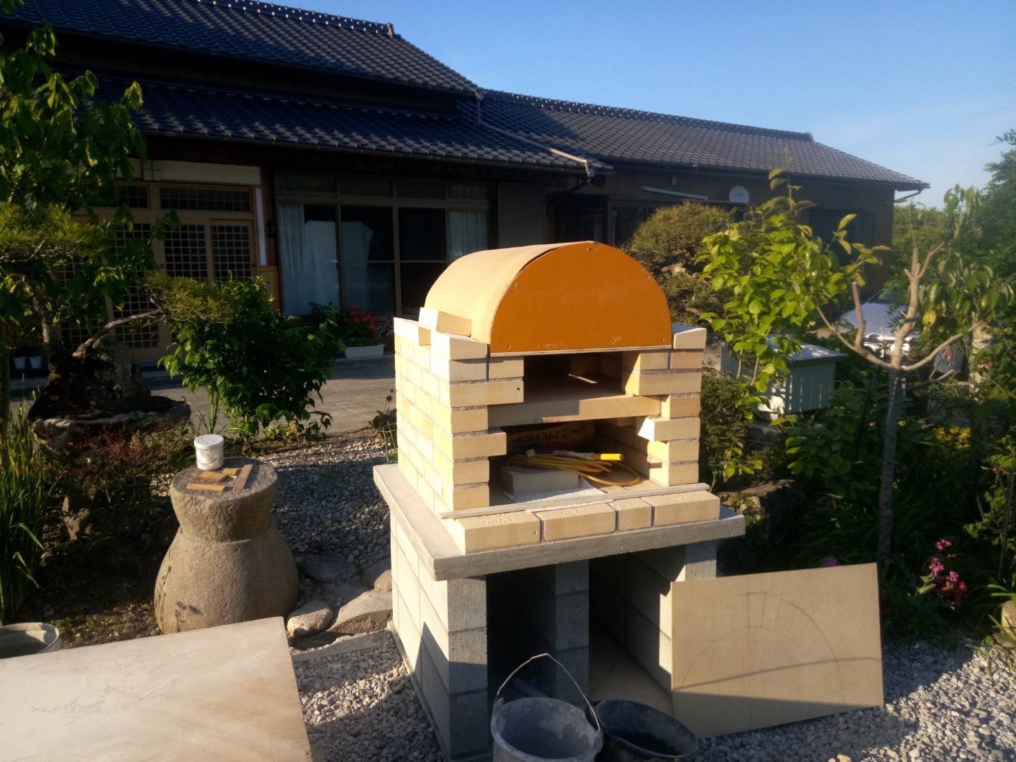 ピザ窯本体のアーチ状の屋根と煙突を、職人が耐火レンガで積み上げている作業風景。豊後高田市のオーダーメイドピザ窯。