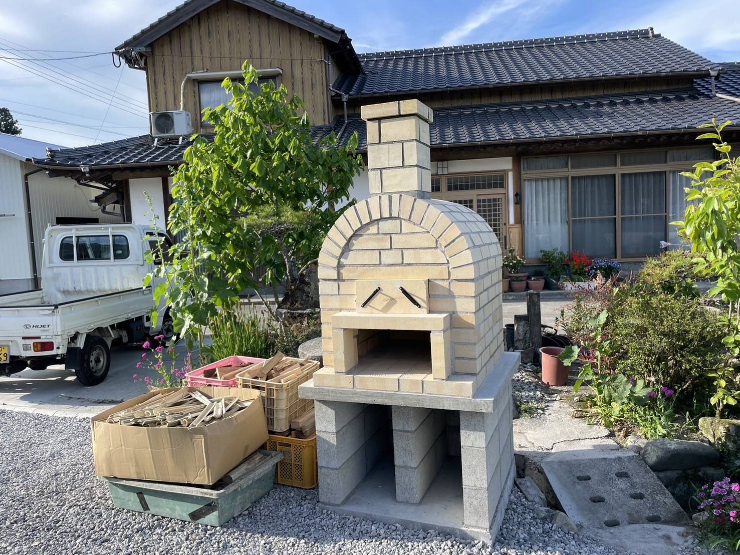 国東市に完成した、レンガ造りの本格的な家庭用ピザ窯。薪で焼いたピザを楽しむ家族の後ろ姿。庭のリフォーム事例。