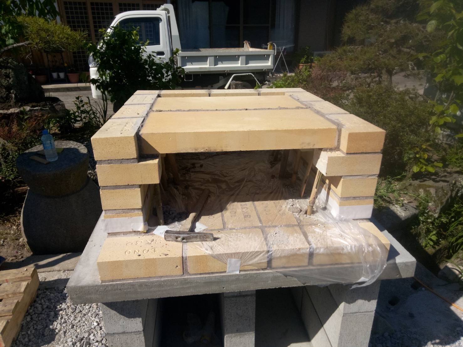 国東市で施工中のピザ窯。職人が特殊な耐火レンガを使い、窯の床面を精密に敷き詰めている写真。ピザ焼きに最適な表面。